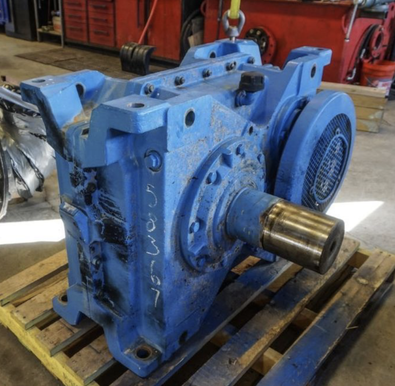 Worn industrial gearbox with oil-stained blue housing on a pallet before repair